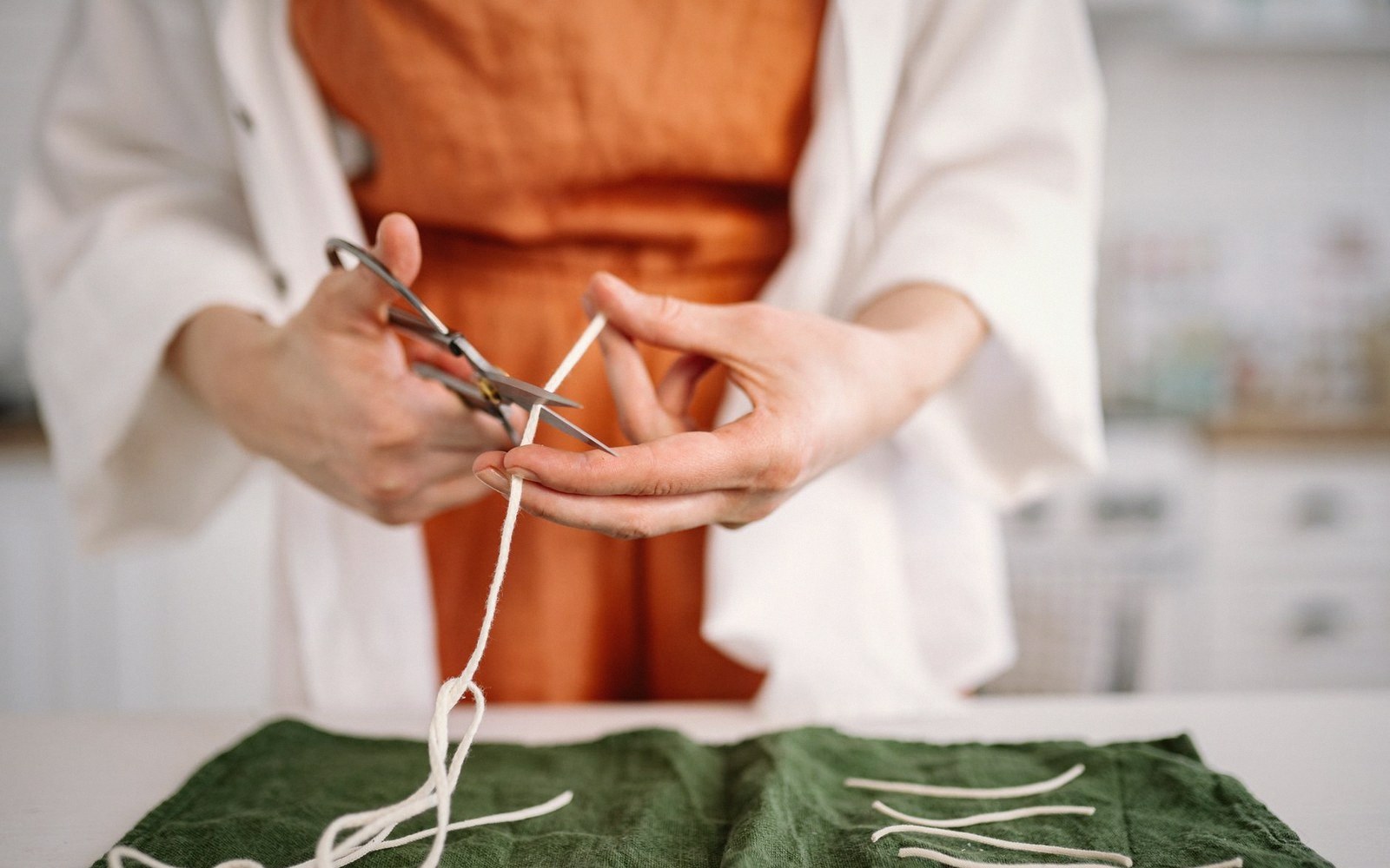 Person cutting a length of white string with scissors over a green cloth