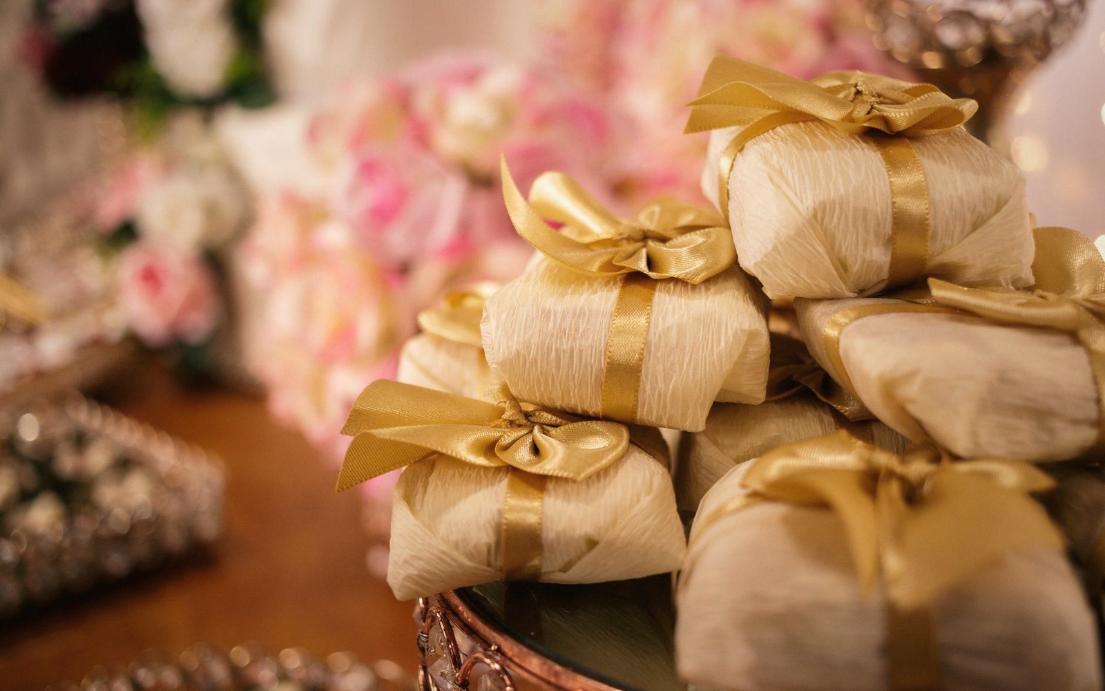 Small favors wrapped in cream paper tied with gold ribbon bows, stacked on a table