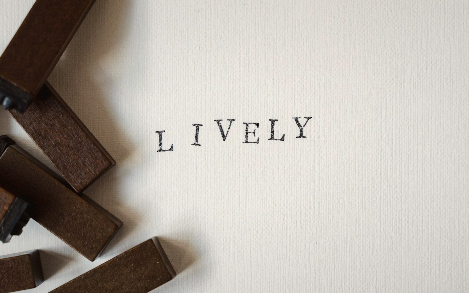 Wooden letter stamps beside the stamped word "lively" on textured paper