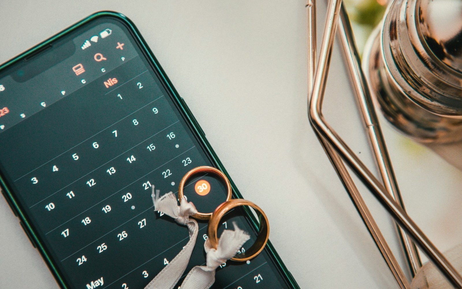 Two gold wedding rings tied with ribbon resting on a smartphone calendar app