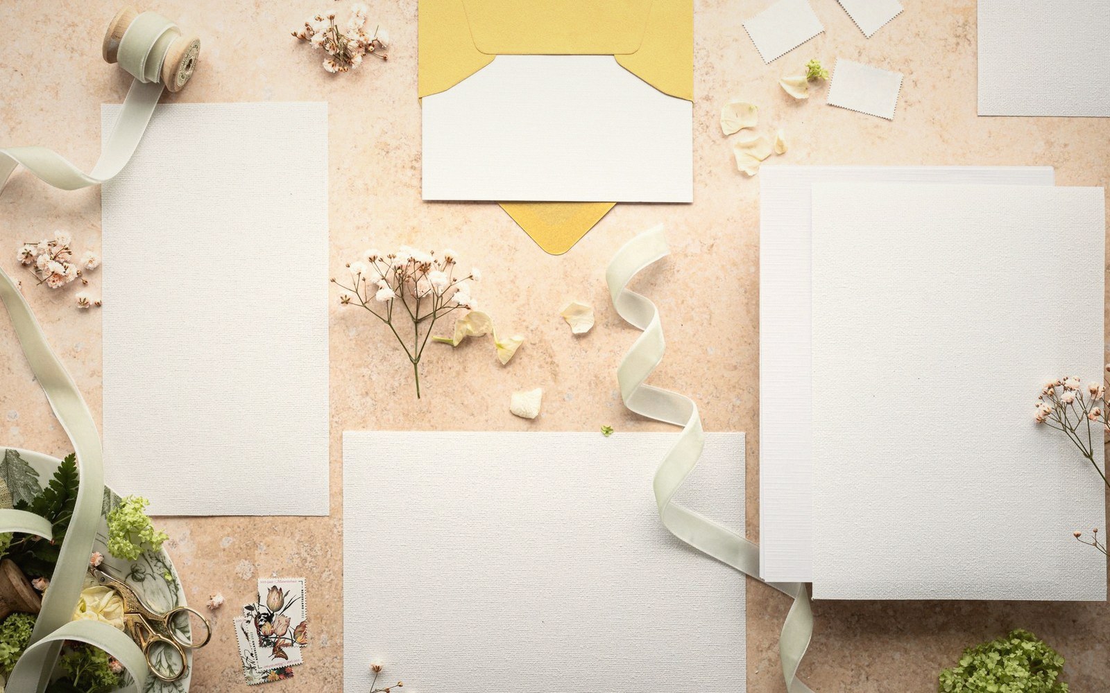 Blank invitation cards, a yellow envelope, ribbon and dried flowers on a table